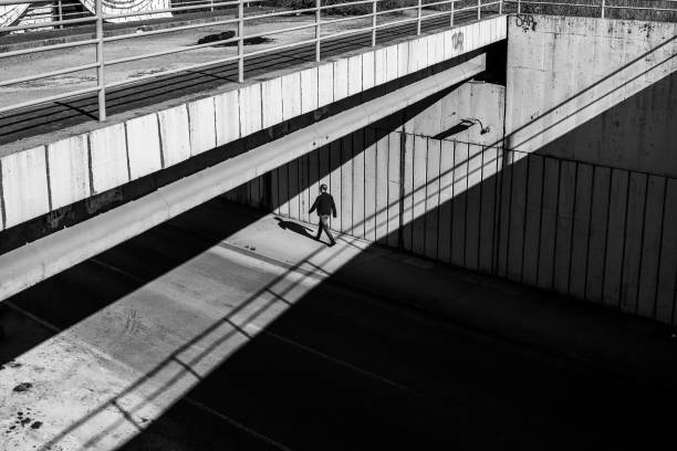 A black and white street scene with a person walking under a bridge