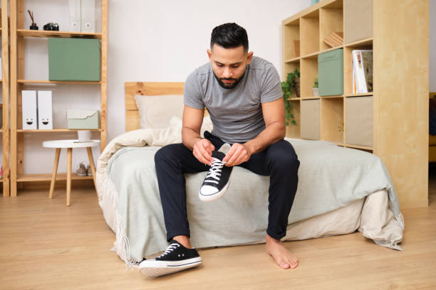istock Young man tying shoelaces on bed in cozy bedroom 2186822407