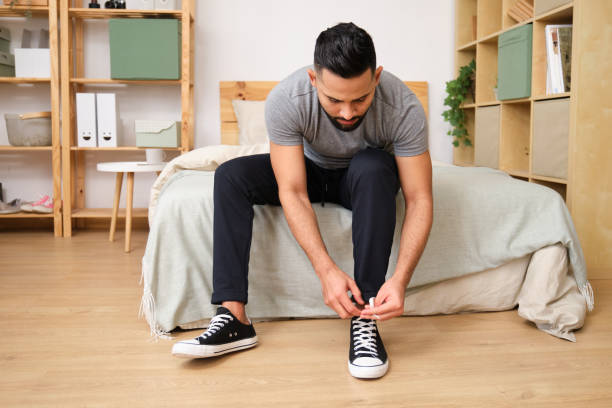 istock Young man tying shoelaces on bed in cozy bedroom 2186823047