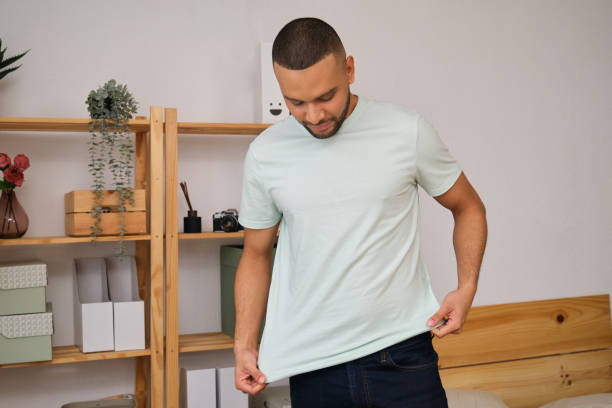 Young man trying on light green t-shirt at home