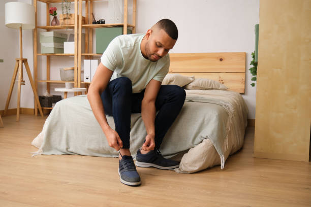 istock Young man tying his shoes while sitting on bed in his bedroom 2186824822
