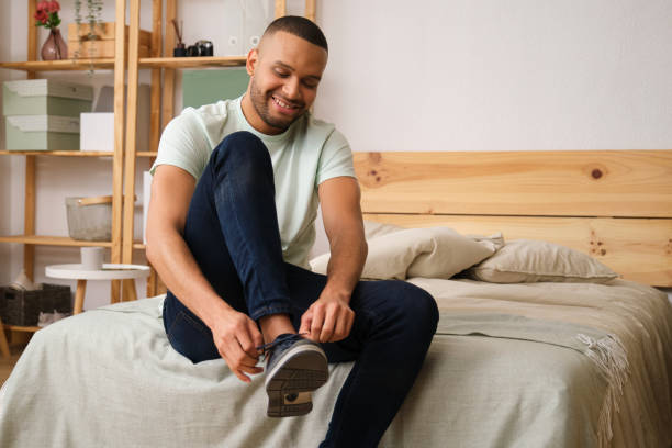 istock Young man tying his shoes while sitting on bed in his bedroom 2186824942