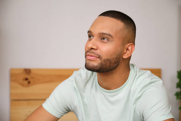 istock Young man smiling and looking away while sitting on bed 2186825134