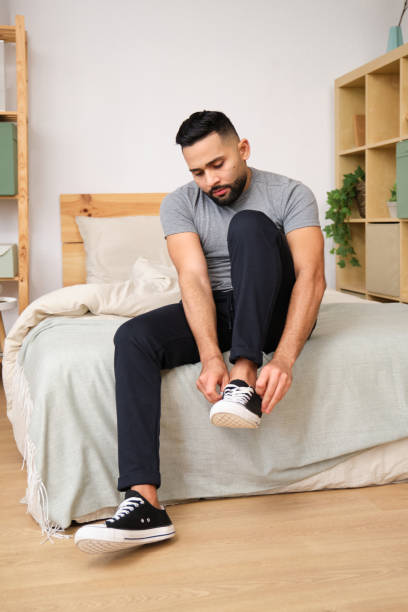 istock Young man tying shoelaces on bed in cozy bedroom 2186826440