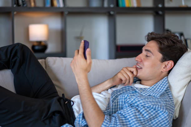 istock Young adult man relaxing on sofa using smartphone at home 2186835600