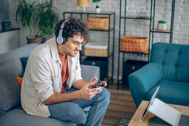 istock Young man is playing video game on digital tablet with headphones using hand controller 2186840119