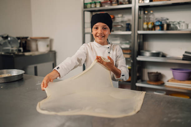 istock Young child girl chef proudly displaying stretched dough in a kitchen. 2186841579