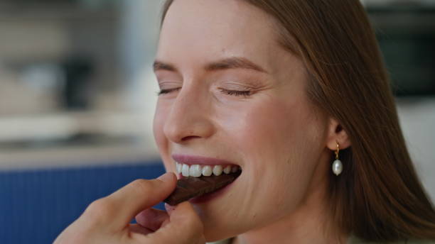 Happy woman biting chocolate closing eyes with satisfied expression closeup.