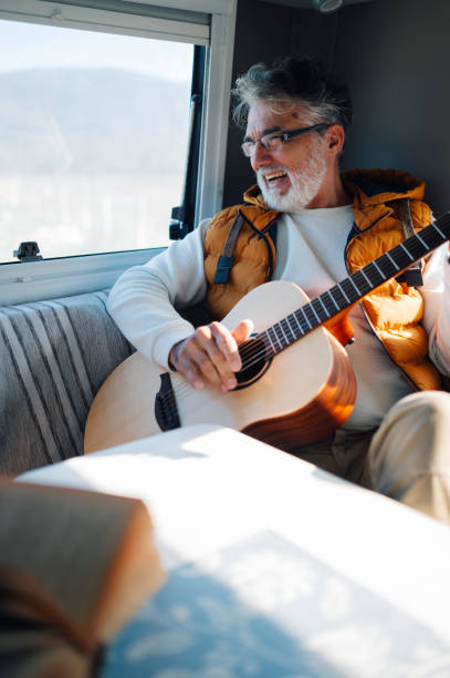 istock Senior man playing guitar inside camper van enjoying carefree alternative lifestyle 2186847493