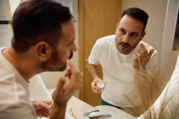 istock Mid adult man applying face cream while looking himself in a mirror. 2186856162