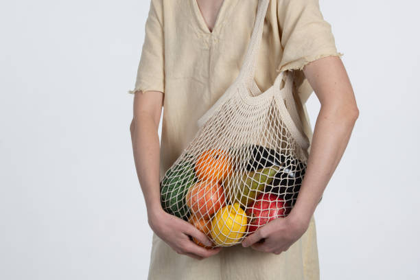 istock A person wearing a simple, natural fabric outfit holds a netted bag filled with assorted organic fruits, showcasing sustainable choices and healthy living 2186857879