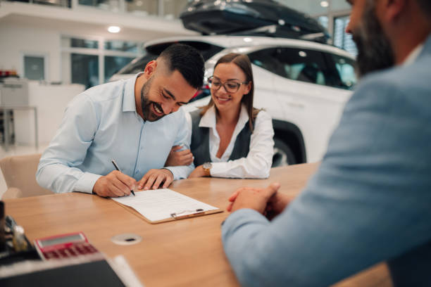 istock Content couple signing car purchase agreement at dealership table. 2186859049