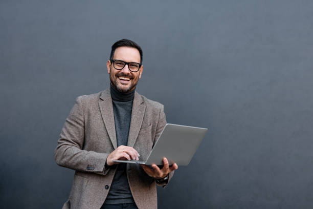 istock Man typing on laptop, smiling with glasses, gray background. 2186864850