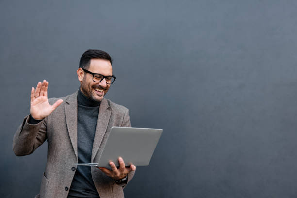istock Man waving with laptop in hand on gray backdrop, smiling face. 2186864851