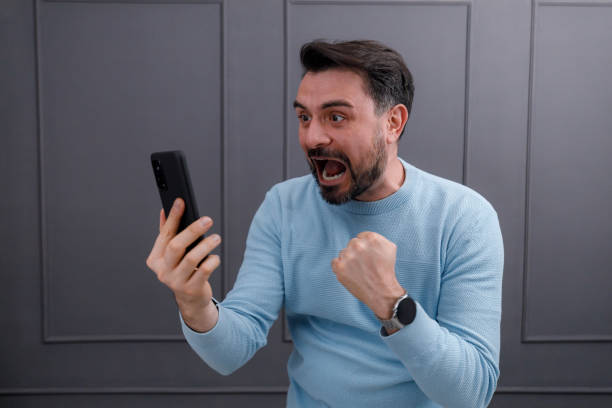 istock Excited man celebrates victory while looking at a smartphone 2186866763