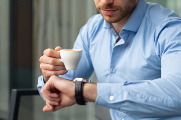 istock Young Businessman Sitting in Cafe, Checking Time While Holding Coffee, in Front of Modern Business Building 2186867671