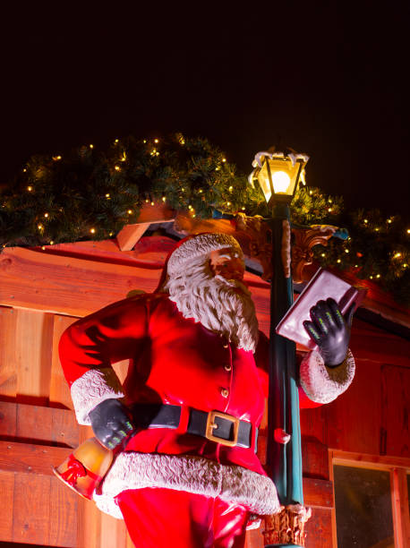 Santa Claus statue reading a book under Christmas lights at night view from below