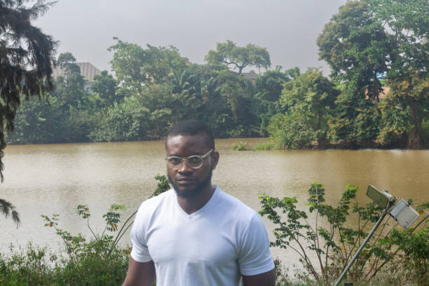 Young adult male 26 years old stands in front of brown colored lake with lush vegetation examplifies a healthy outdoorsy lifestyle