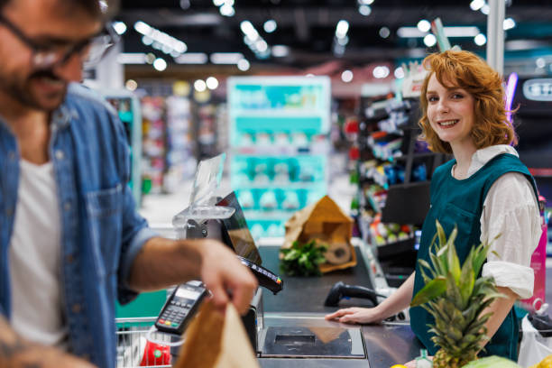 istock Smiling cashier assisting customer paying at checkout in supermarket 2186871982