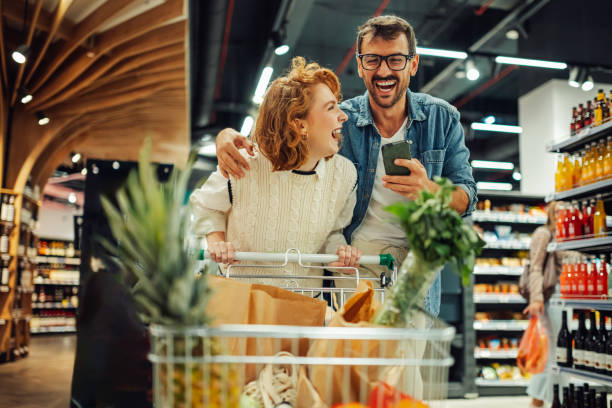 istock Happy couple using smartphone and laughing while shopping in supermarket 2186871993