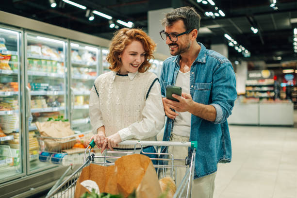 istock Happy couple using smartphone while shopping groceries in supermarket 2186872025
