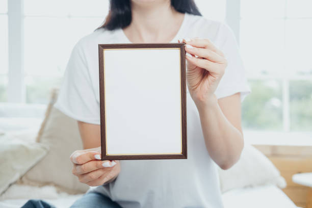 istock Person holding an empty wooden picture frame in a cozy, sunlit indoor setting 2186876621