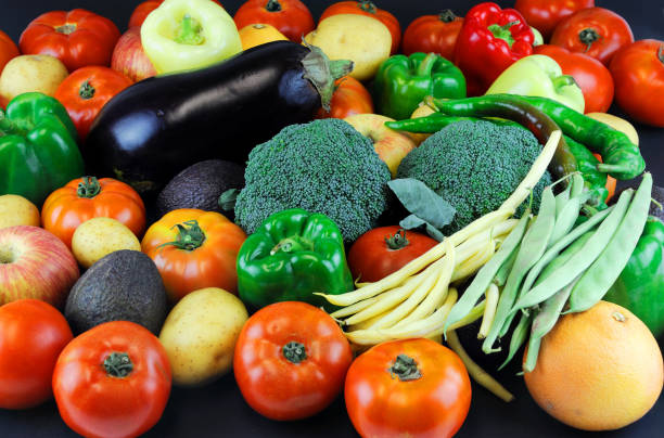 In Paris, France at the outdoor Montparnasse Market a variety of vegetables are for sale. Green broccoli, red and green bell peppers and eggplant are displayed on the vendor’s table.
