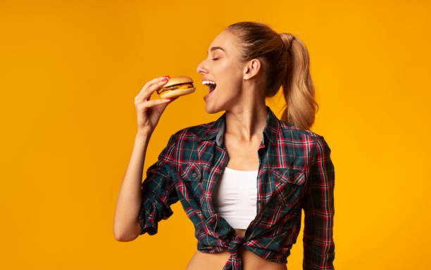 istock Slim Woman Eating Burger Having Cheat Meal Day, Yellow Background 2186888397