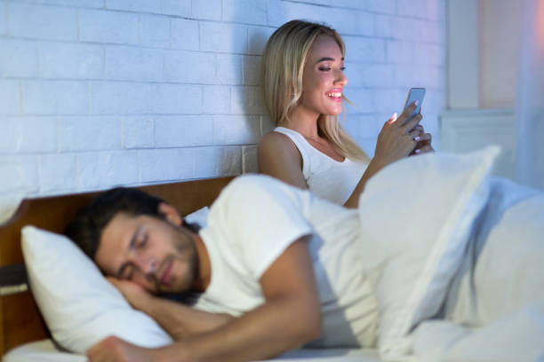 istock Cheating Wife Chatting On Cellphone While Husband Sleeping In Bedroom 2186894885