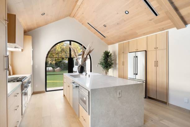 Modern kitchen with wooden cabinetry and arched window.