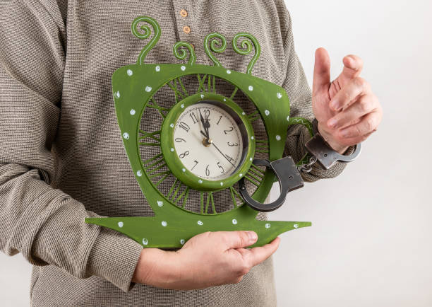 A clock in the shape of a tea cup is handcuffed in a man's hand