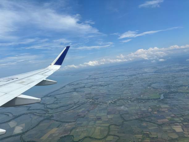 Aerial view from an airplane window, featuring the wing in the foreground surrounded by a vast blue ocean under a partly cloudy sky.