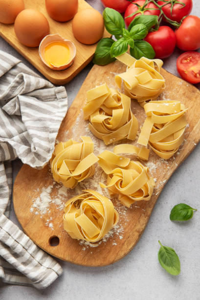 istock Uncooked tagliatelle pasta nests with basil, tomatoes and eggs on wooden cutting board 2186913988