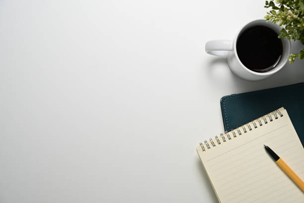 White office desk with cup of coffee, notepad and plant. Top view, Flat lay.
