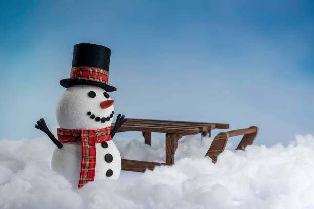A happy snowman in a top hat and scarf, arms up and ready for winter fun! Posing with a sled on a snowy background and bright blue sky.