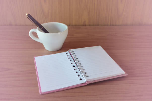 Still life,open notebook with blank pages next to cup of coffee on wooden table.