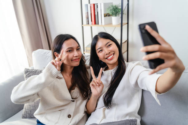 istock Two women are sitting on a couch and taking a selfie 2186920403
