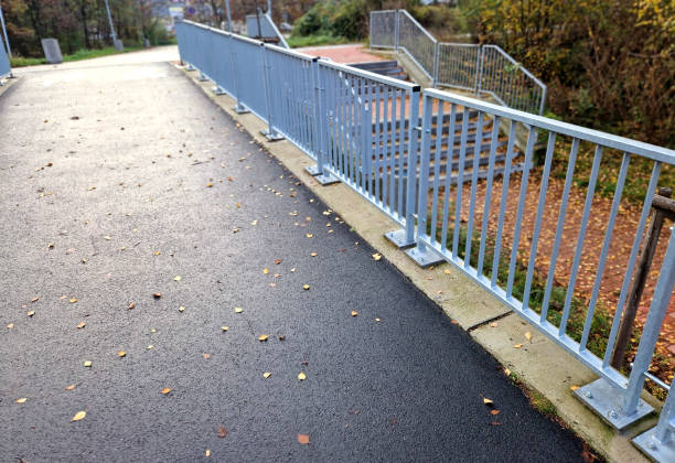 bridge railing with vertical fence posts anchored into the ground with four concrete screws. the railing is fixed from the side of the bridge into the concrete.