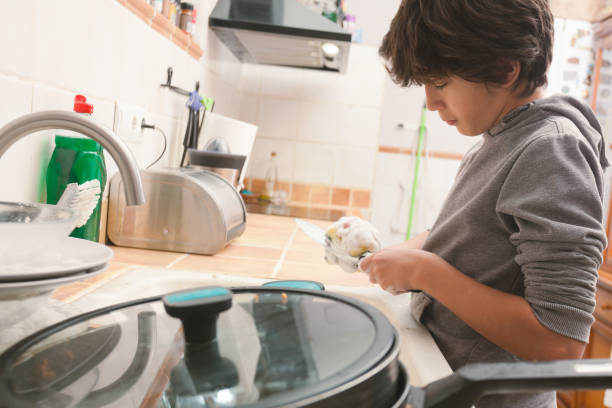 istock A boy washes dishes with a brush in a rustic kitchen. 2186929173