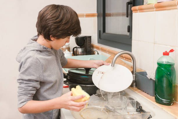 istock A boy washes the dishes in the kitchen with water, soap and a sponge. 2186929264