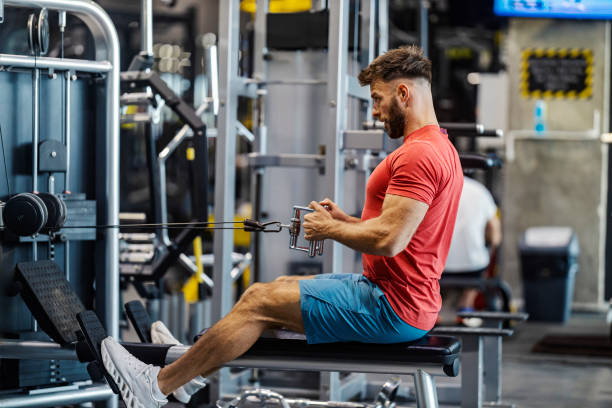 Side view of strong bodybuilder doing strength workouts with effort on cable machine.