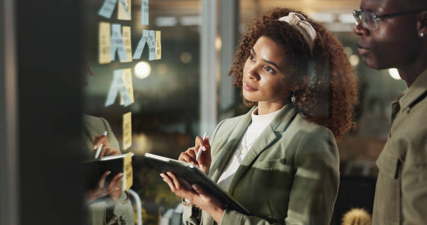 istock Creative people, tablet and thinking at window for planning, collaboration or brainstorming with sticky notes. Workshop, design team or tech in agency for ideas, problem solving or moodboard on glass 2186942272