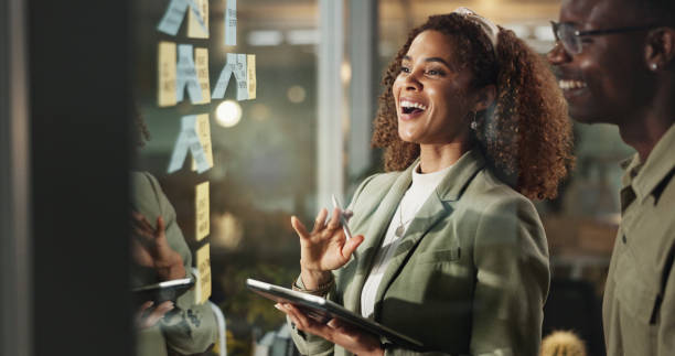 istock People, tablet and happy at glass for planning, deadline progress and sticky notes at night. Business team, tech and laugh in dark office for productivity, project development and ideas on window 2186942275