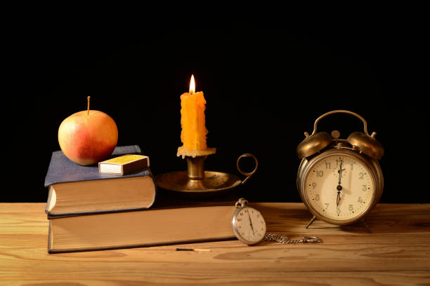 Still life, alarm clock, candlestick, candle and books on the table