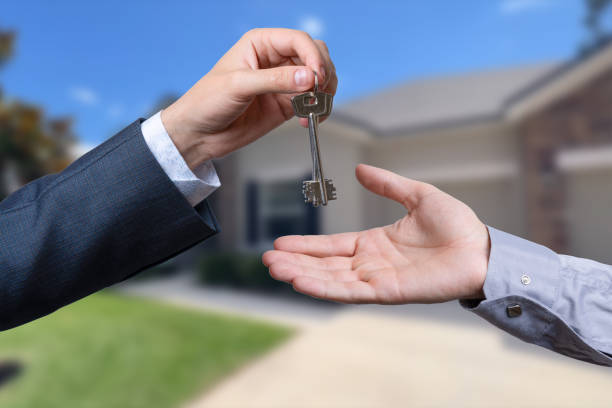 istock A hand giving a key to another hand. House in the background. 2186948262