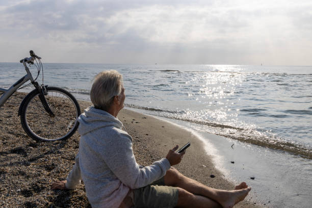 istock Mature man uses phone on water's edge, with bicycle 2186952747