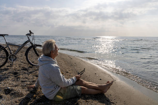 istock Mature man uses phone on water's edge, with bicycle 2186952773
