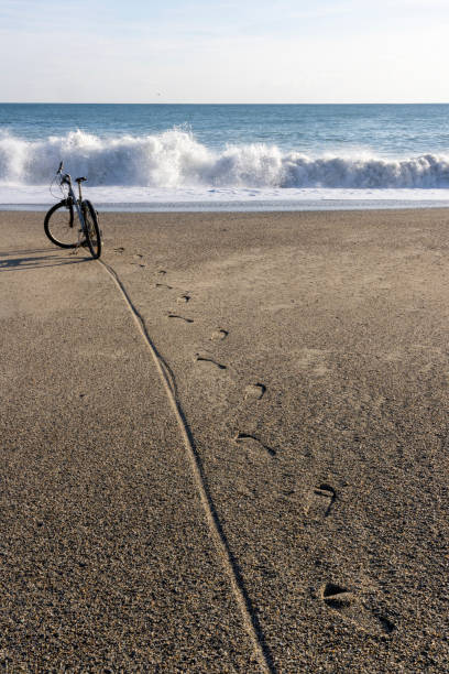 Scenic view of parked bicycle on beach near surf, track leading through sand to bicycle and surf