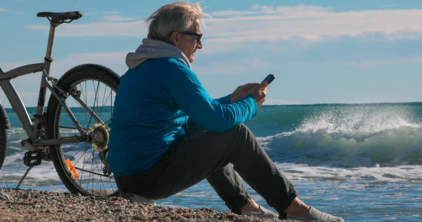 istock Mature man uses mobile phone on water's edge, with bicycle 2186953605