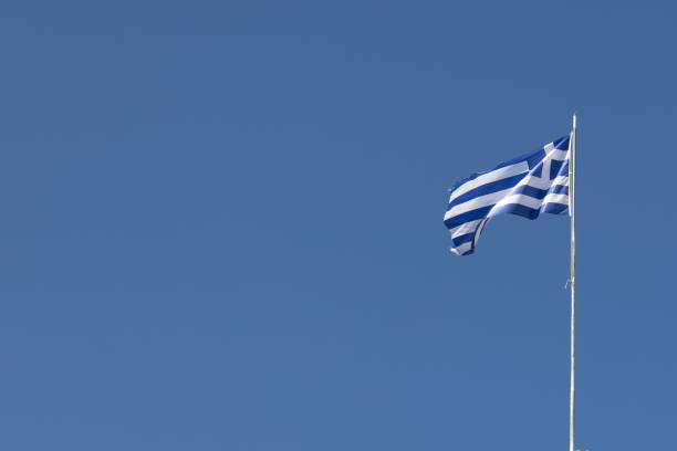The Greek national flag waving gracefully against a bright blue sky representing freedom and cultural pride